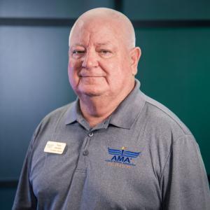 Man in gray polo shirt with a blue logo, smiling slightly, against a teal background.