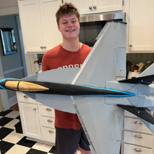 Teen with a large model jet plane in a kitchen setting.