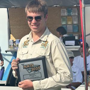 Young man smiling, holding a framed certificate outdoors.