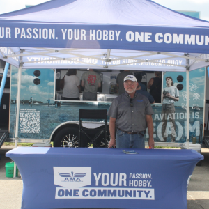 Man standing at an AMA booth with banners; a trailer in the background.