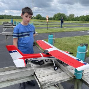 Boy in blue shirt with red-and-white model airplane outdoors.