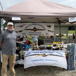 Vendor booth with model aircraft, banner, and man in front.