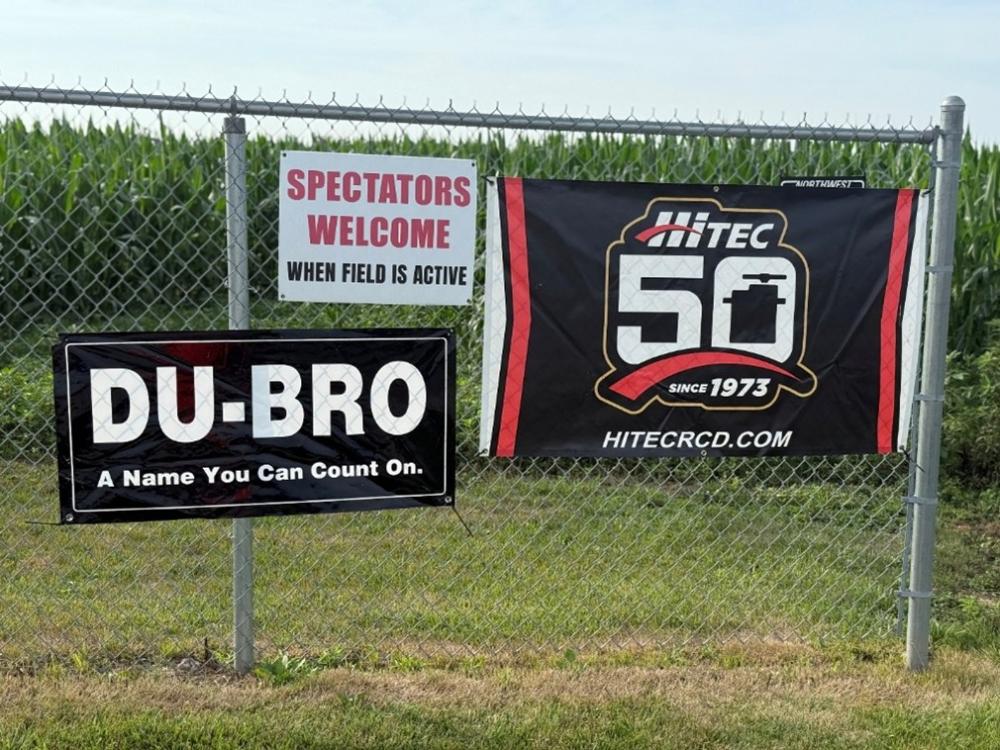 Fenced area with banners for DU-BRO and HITEC, grassy field in the background.