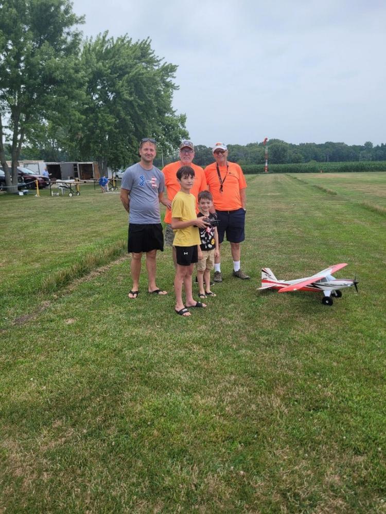 Four people stand on a grassy field with a model airplane.