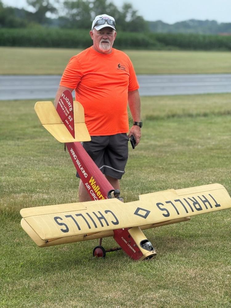 Man with a large yellow and red model airplane on grass.