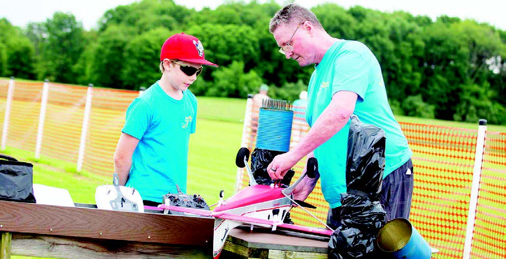 Man and boy preparing a small red airplane outdoors.