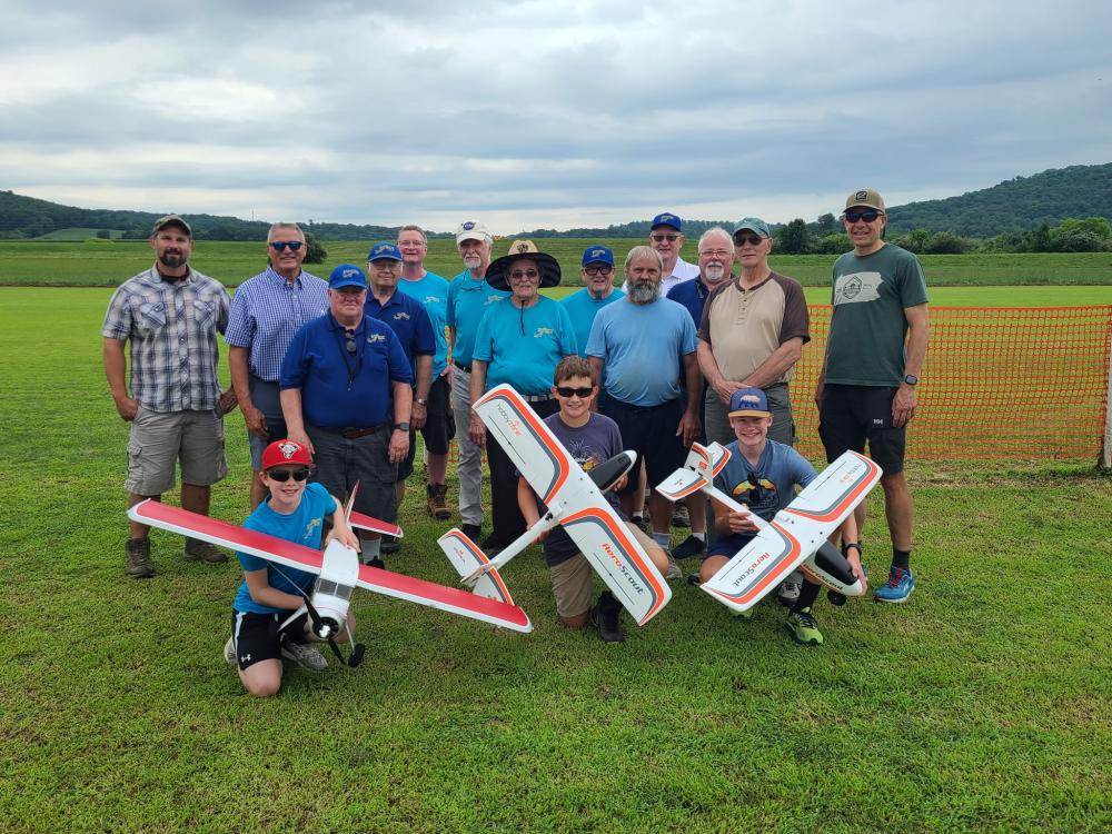 Group photo of people on grass, with three holding model airplanes.
