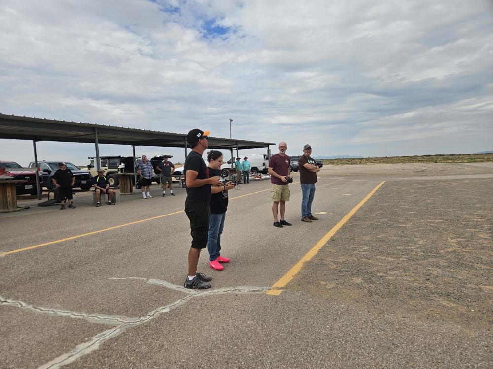 Four people standing on asphalt near a canopy under a cloudy sky.