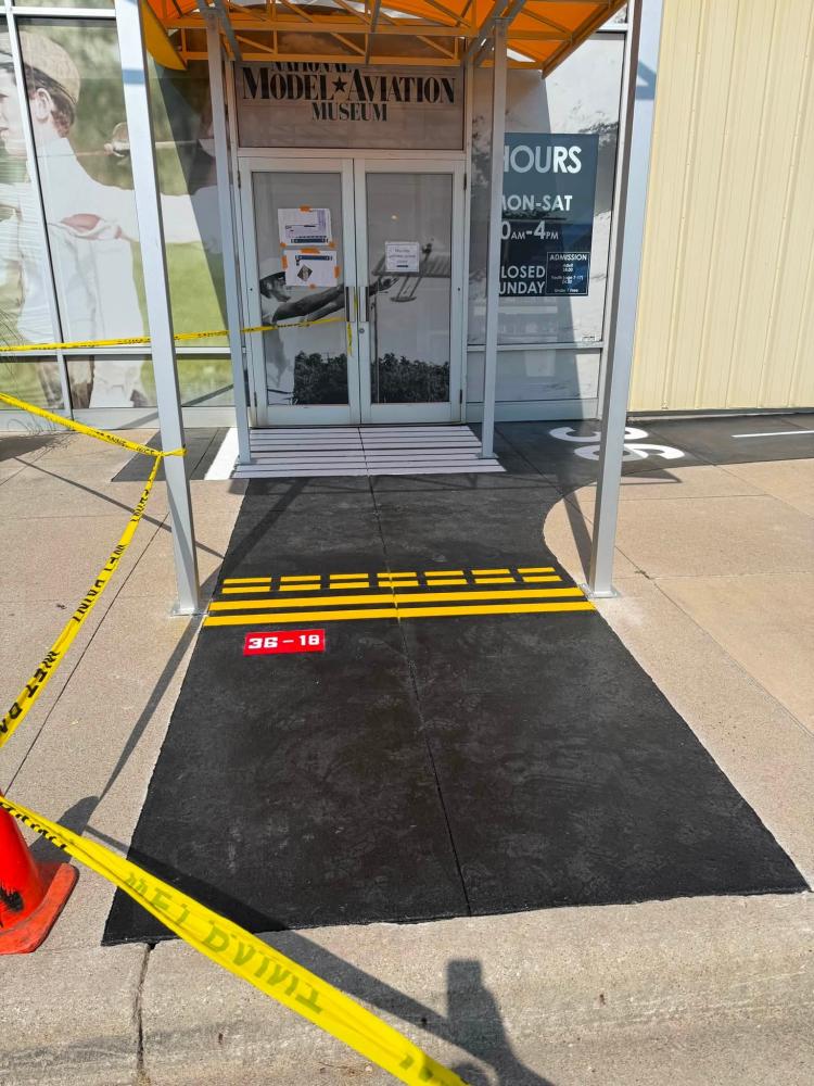 Black ramp with yellow caution stripes leads to a glass door entrance.