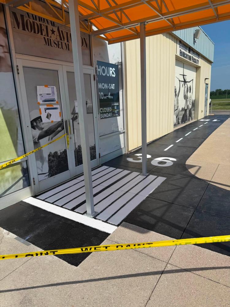 Museum entrance with runway-themed ramp and wet paint caution tape.