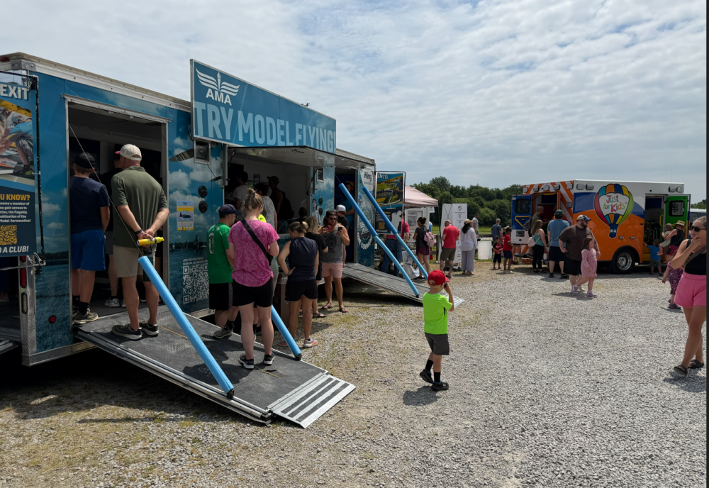 People standing outside trailers and a food truck at an outdoor event.
