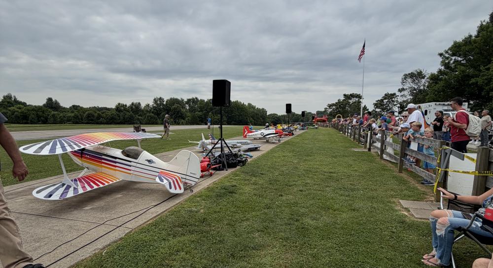 Colorful stunt planes on a grassy field, surrounded by spectators and a cloudy sky.