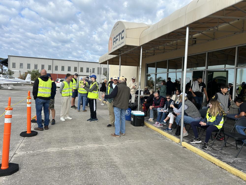 Group of people in safety vests gathering outside an aviation building.