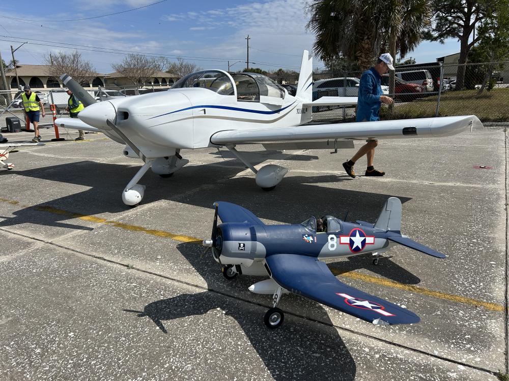 Small model plane beside larger real plane on an airfield.